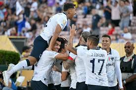 Jogadores do CF Monterrey celebram um gol em grupo, abraçados, durante a partida contra o Urawa Red Diamonds no Mundial de Clubes da FIFA 2025. A imagem transmite união e alegria, com o gramado verde e o estádio ao fundo.